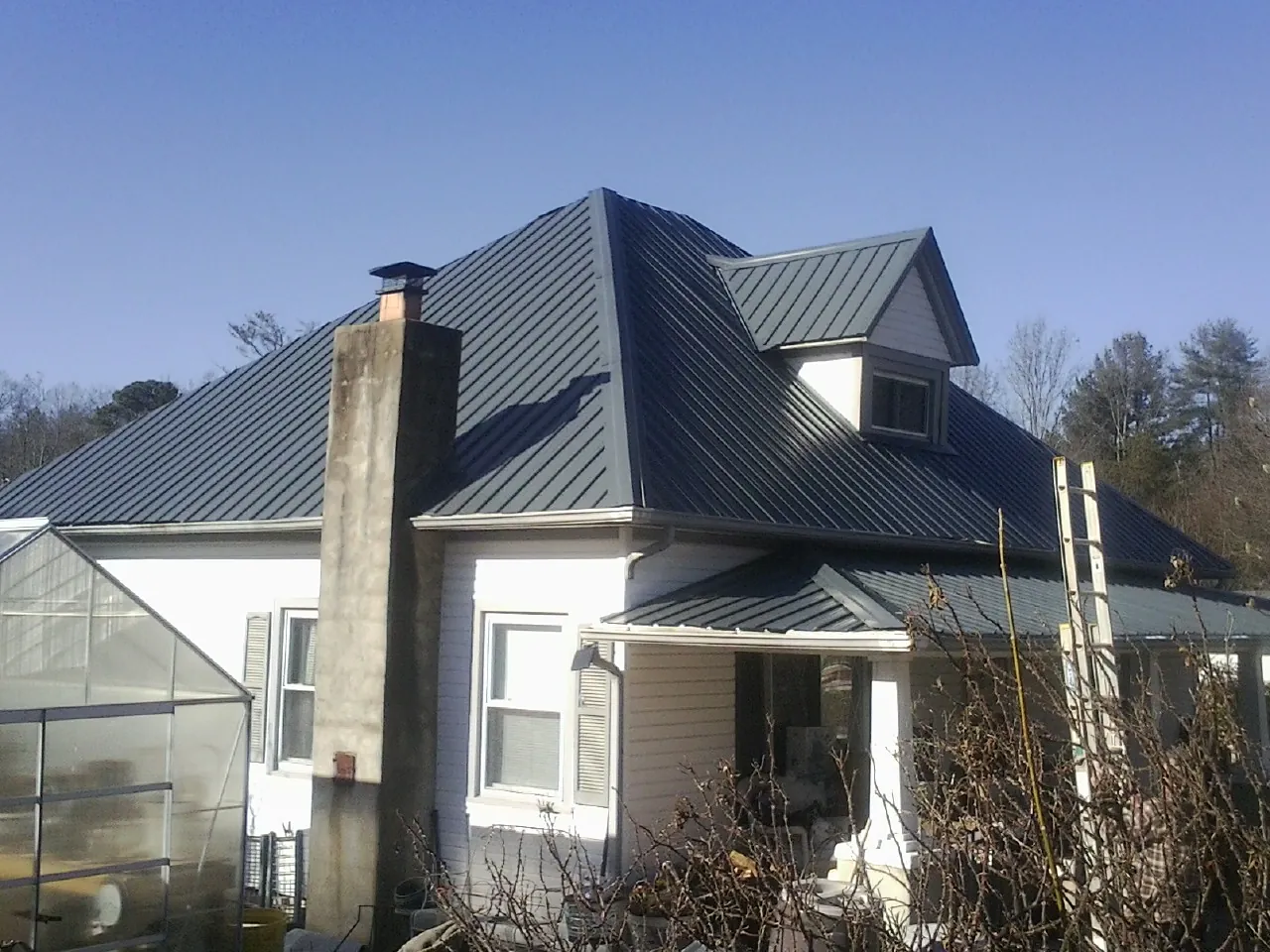 Dark blue standing seam metal roof on a white farmhouse with dormer — Slate & Tile Roof Repair by Roofing Brothers in Wilmore