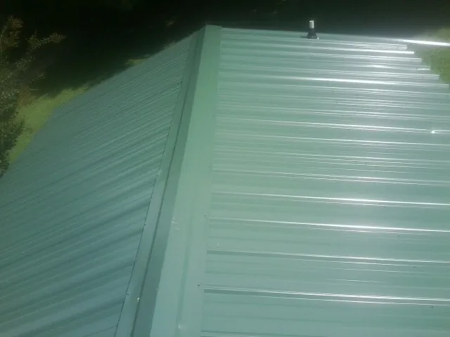 New green metal panels meeting at the ridge of a roof — Flat Roof Repair work by our crew in Wilmore