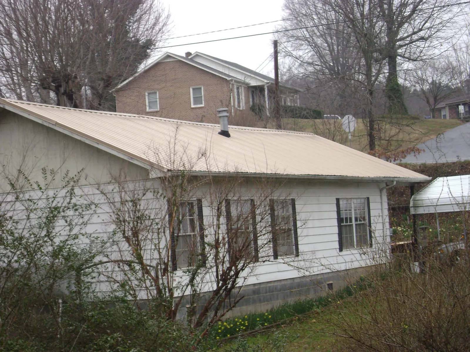 Tan metal roof on a white sided house set into a hillside — Commercial Roofing by Roofing Brothers in Wilmore