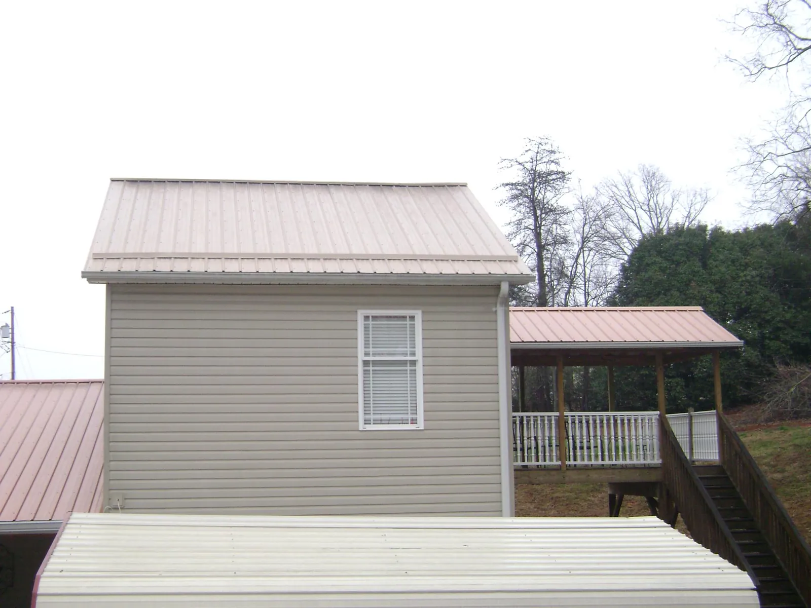 Tan metal roofs on a two story addition and attached porch, from a Roof Replacement job in Wilmore
